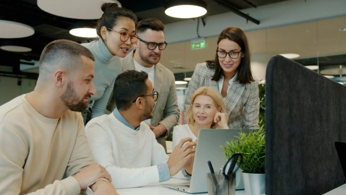 Diverse team collaborating around a laptop in office.